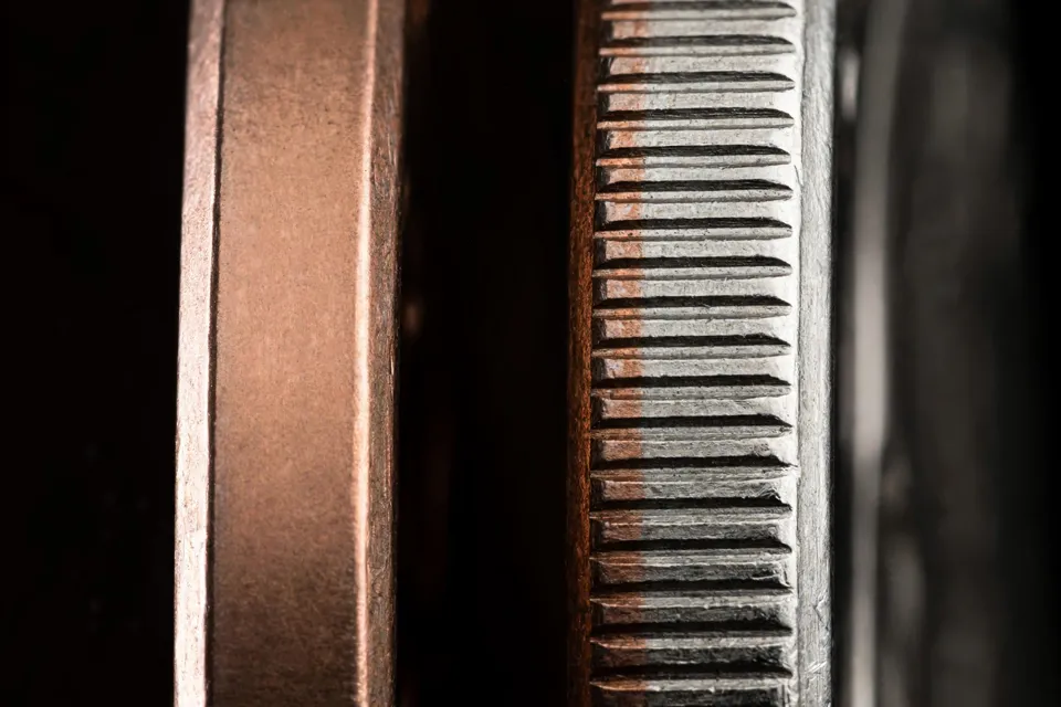 close-up comparing the smooth plain edge of a broadstruck coin with the reeded edge of a normal coin