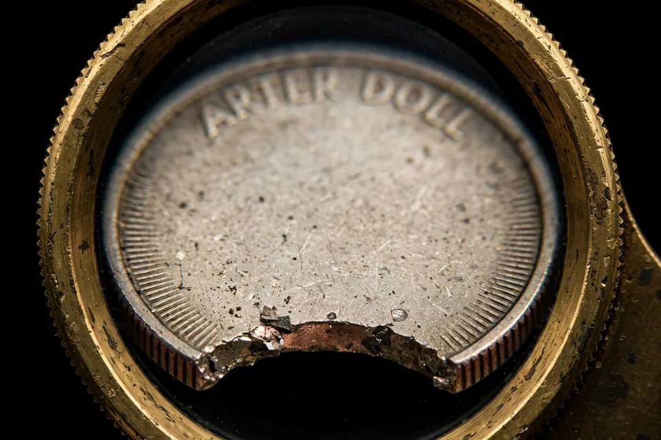 Clipped planchet coin edge under a brass magnifying loupe showing the rough cut-and-tear texture of a genuine clip