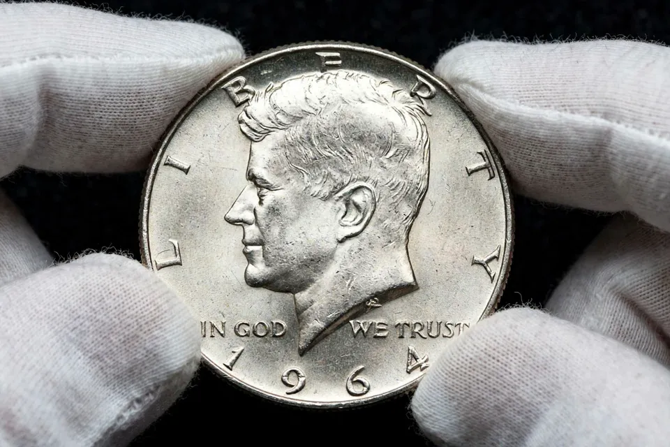 1964 Kennedy half dollar obverse close-up — Kennedy profile with 1964 date in white cotton gloves
