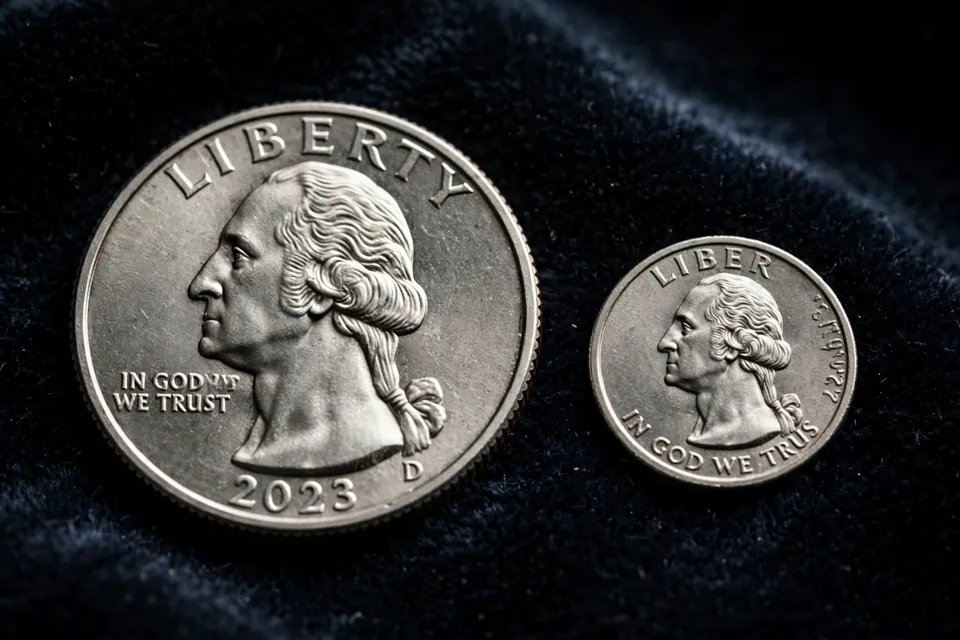Normal Washington quarter beside a smaller quarter design struck on a nickel planchet, the error coin visibly smaller with lettering cut off at the rim